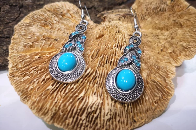 boucles d'oreilles fantaisie blanches et bleues posées sur un support naturel en bois