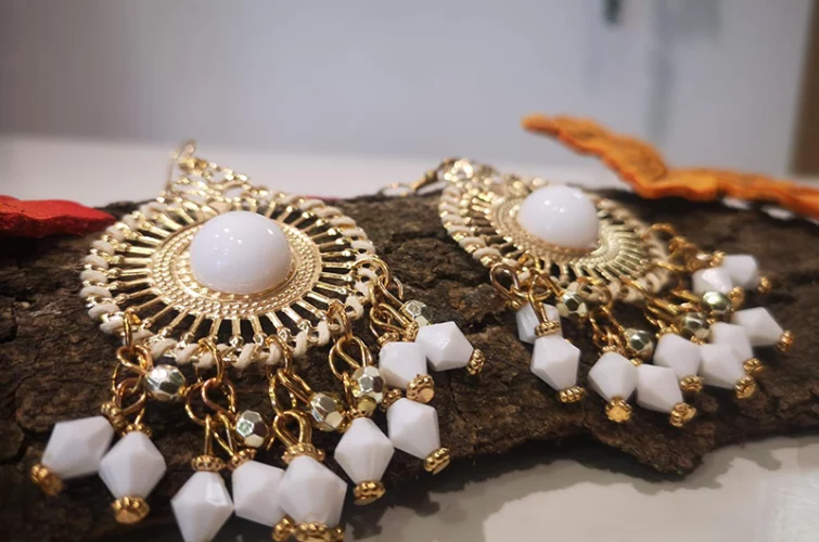 boucles d'oreilles fantaisie blanches et dorées posées sur une écorce d'arbre